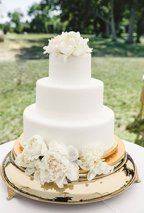 A three-tiered white wedding cake with piped details and fresh flowers created by Confectionery Designs.