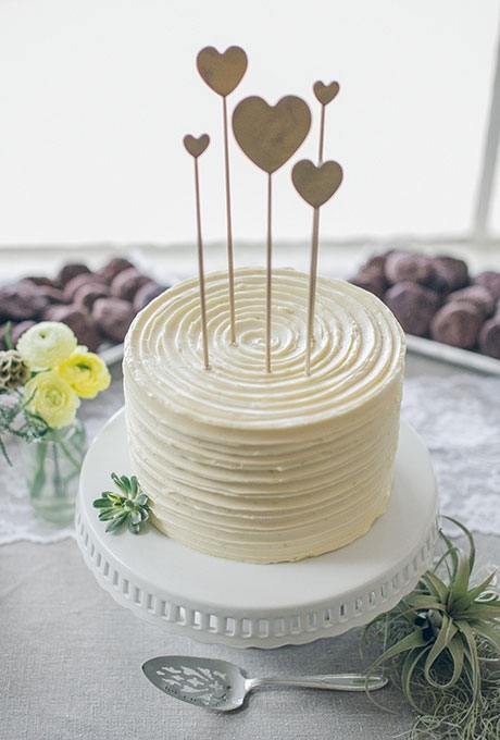 A simple one-tier white wedding cake with heart toppers created by Cake Monkey Bakery. A simple one-tier white wedding cake with heart toppers created by Cake Monkey Bakery.